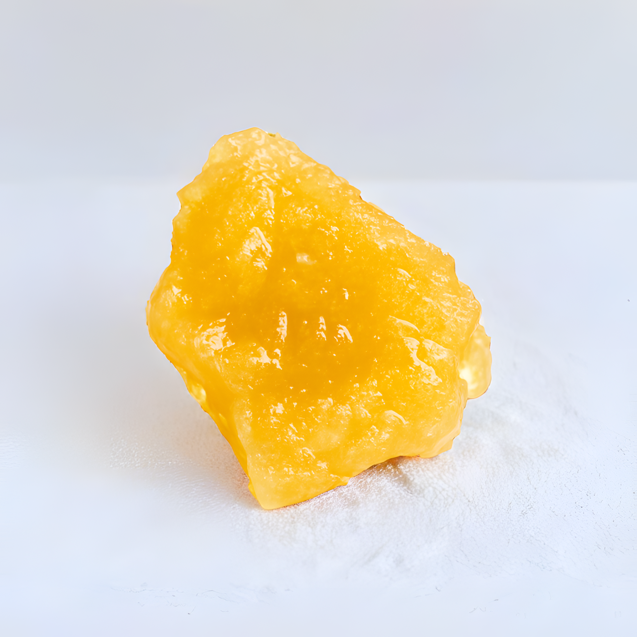 Gelbliche, glänzende Live Resin CBD Dab von 1g auf weißem Hintergrund, zeigt die Textur und Reinheit des Produkts.