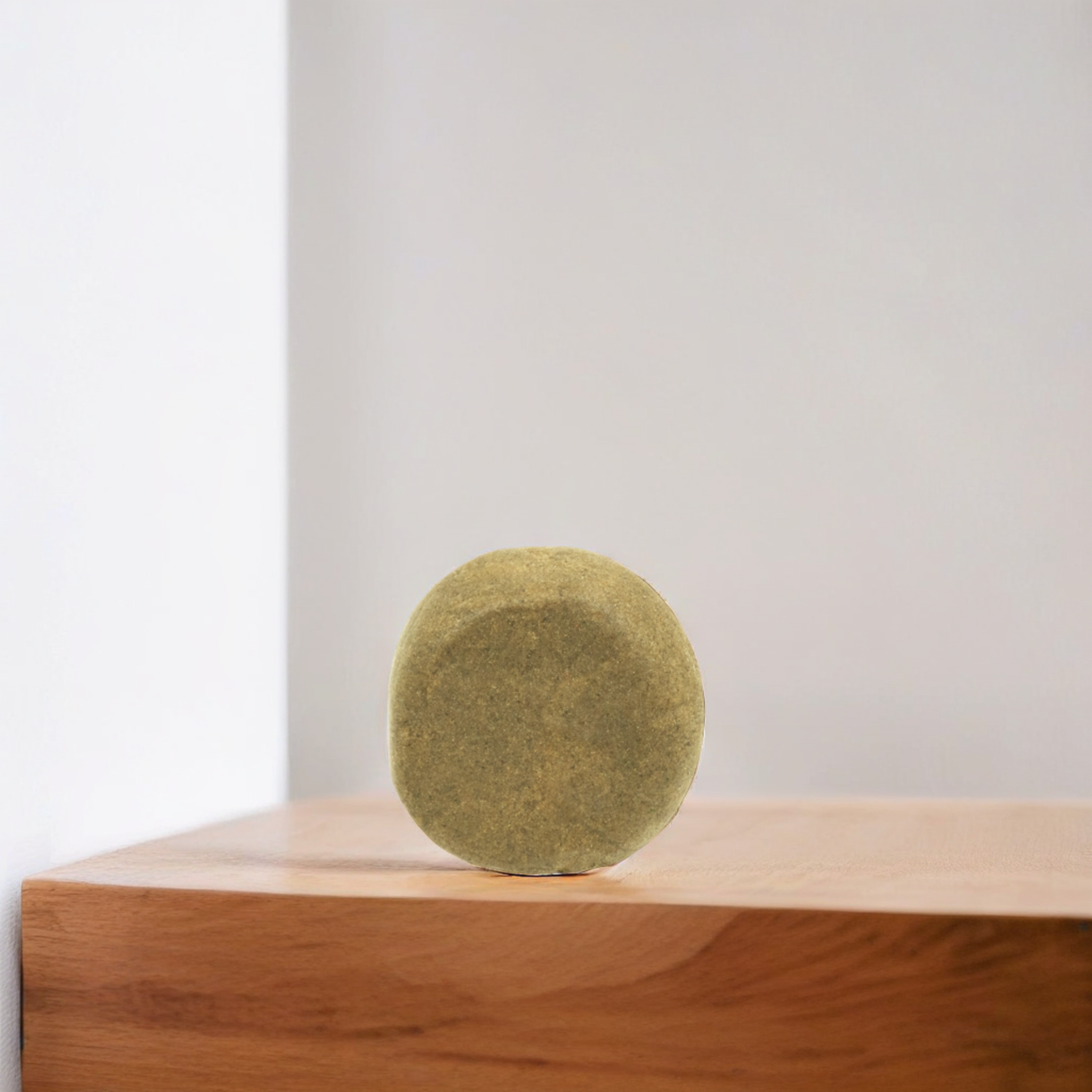 Morceau de hash CBD Zero Zero de forme ronde et poudreuse de Green Passion sur une surface en bois, montrant la texture poussiéreuse et la finition de qualité.
